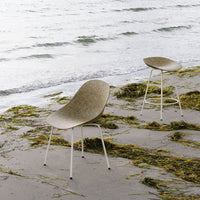 "Two curved chairs in a soft beige color with textured patterns, set against a serene beach backdrop."