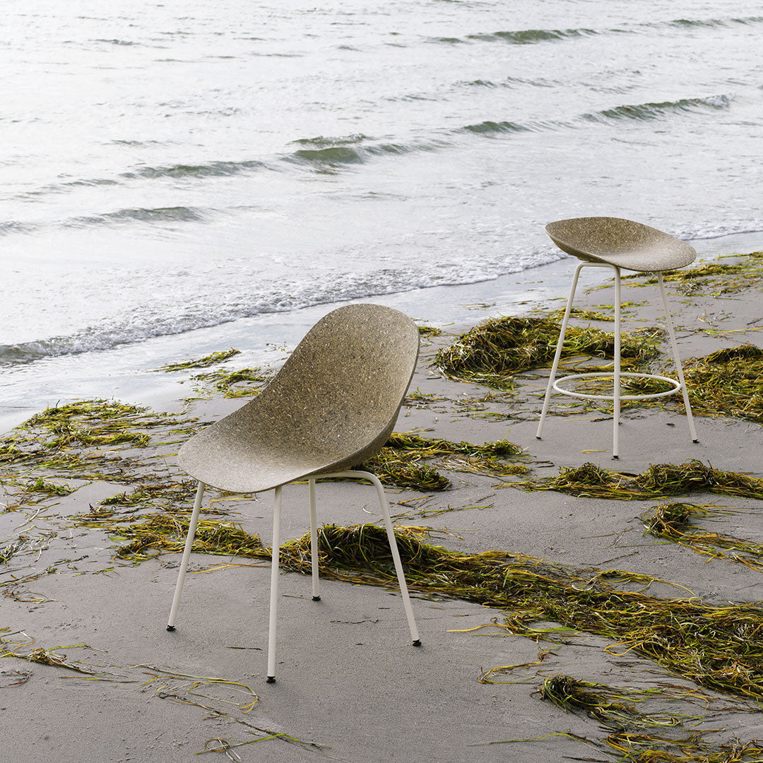"Two curved chairs in a soft beige color with textured patterns, set against a serene beach backdrop."