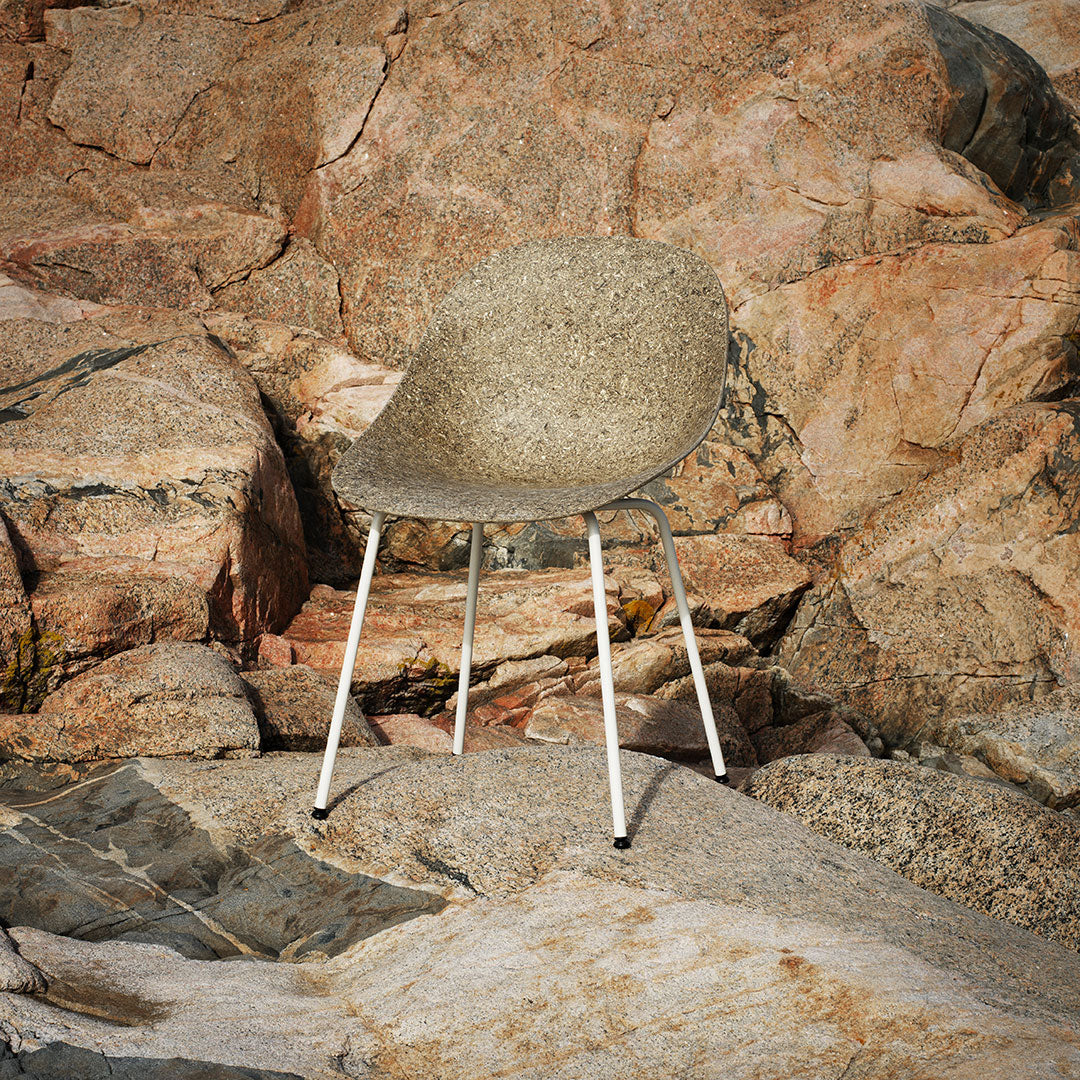 Textured gray chair with a light speckled pattern, featuring white legs, set against a rocky natural backdrop.
