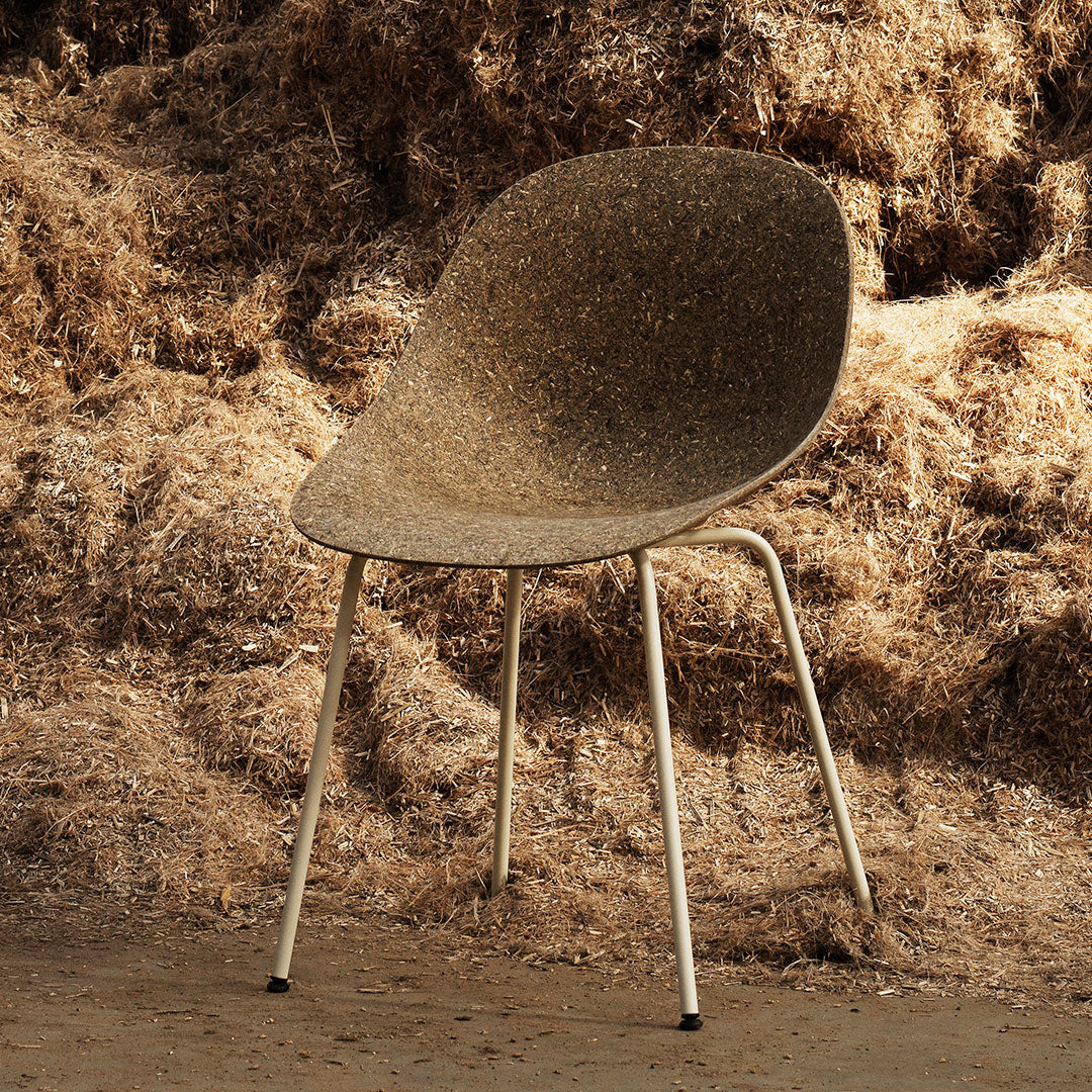 Brown speckled chair with a smooth, curved seat and white metal legs, set against a rustic, textured backdrop.