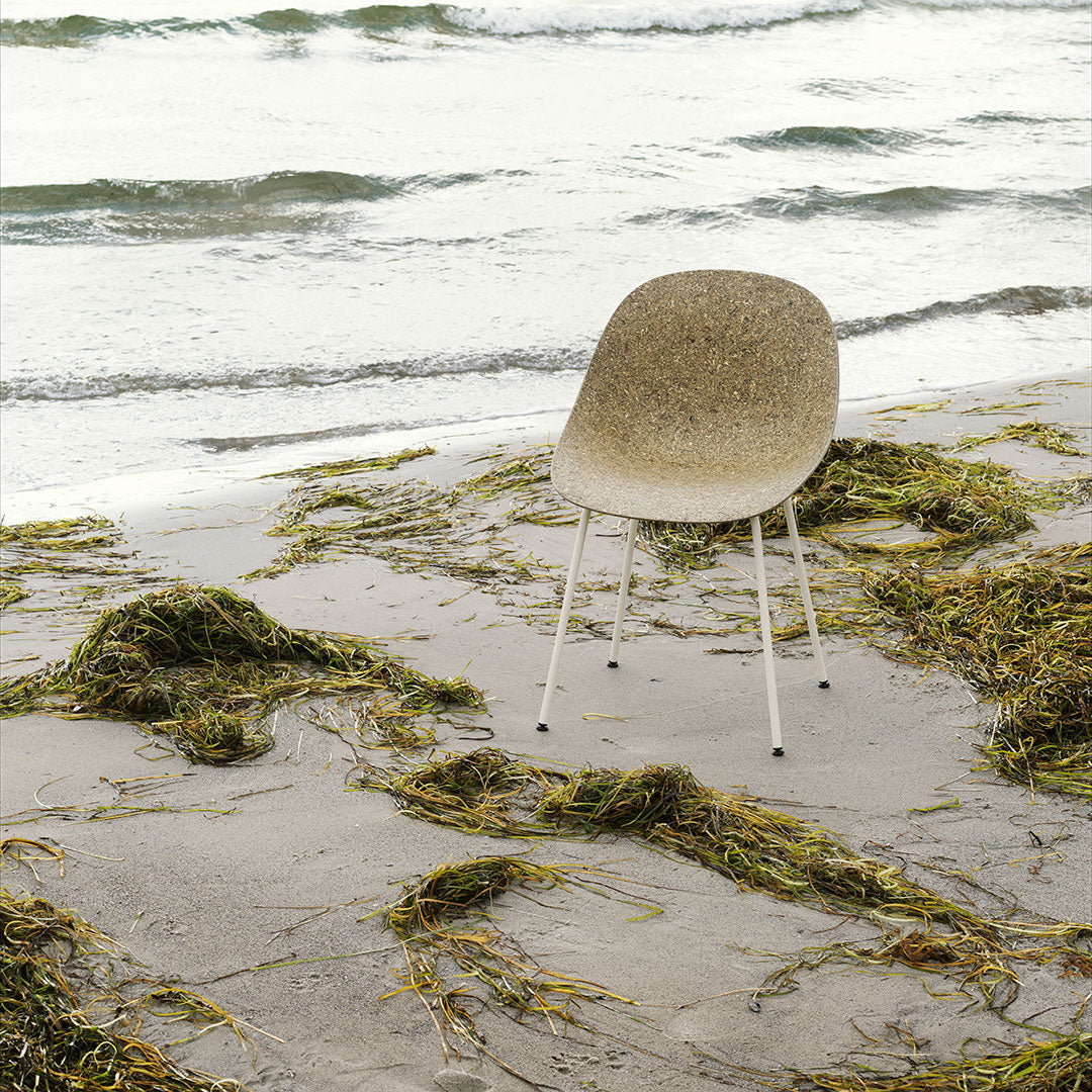 Beige and olive green patterned chair against a scenic beach backdrop with waves and seaweed.