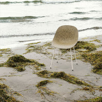 Beige and olive green patterned chair against a scenic beach backdrop with waves and seaweed.