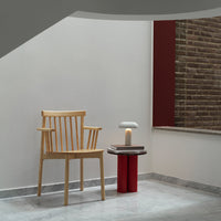 Light wood chair, red side table, minimalistic design; neutral wall with textured brick accents. Modern, stylish interior.