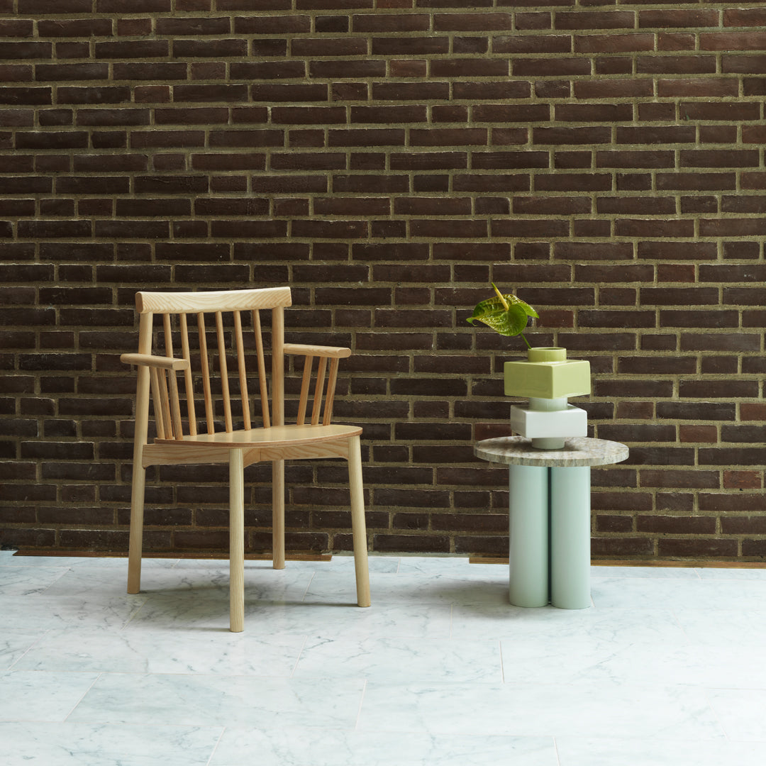 Light wood chair paired with a pastel green and white accent table, against a textured dark brick wall backdrop.