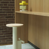 Minimalist light cream stool with a circular wooden top, set against a warm wooden backdrop and brick wall.