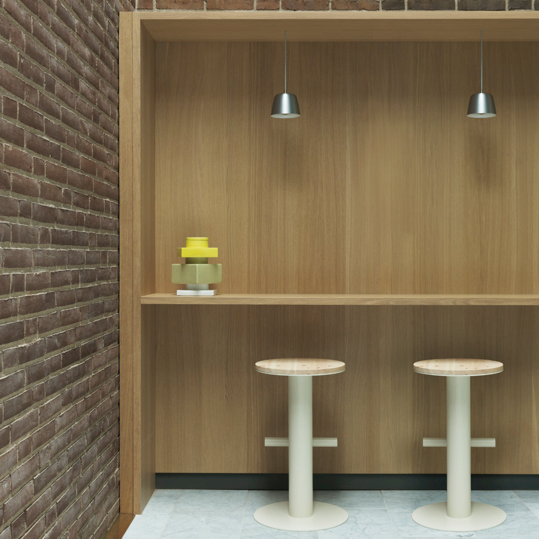"Modern wooden bar with light-colored stools, yellow decor, and subtle gray tile against a rustic brick wall."
