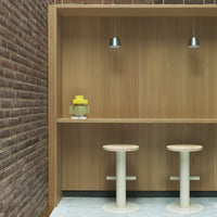 "Modern wooden bar with light-colored stools, yellow decor, and subtle gray tile against a rustic brick wall."