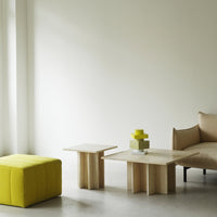 Yellow ottoman, natural wood tables, and soft beige couch against a neutral wall, creating a modern, minimalist aesthetic.