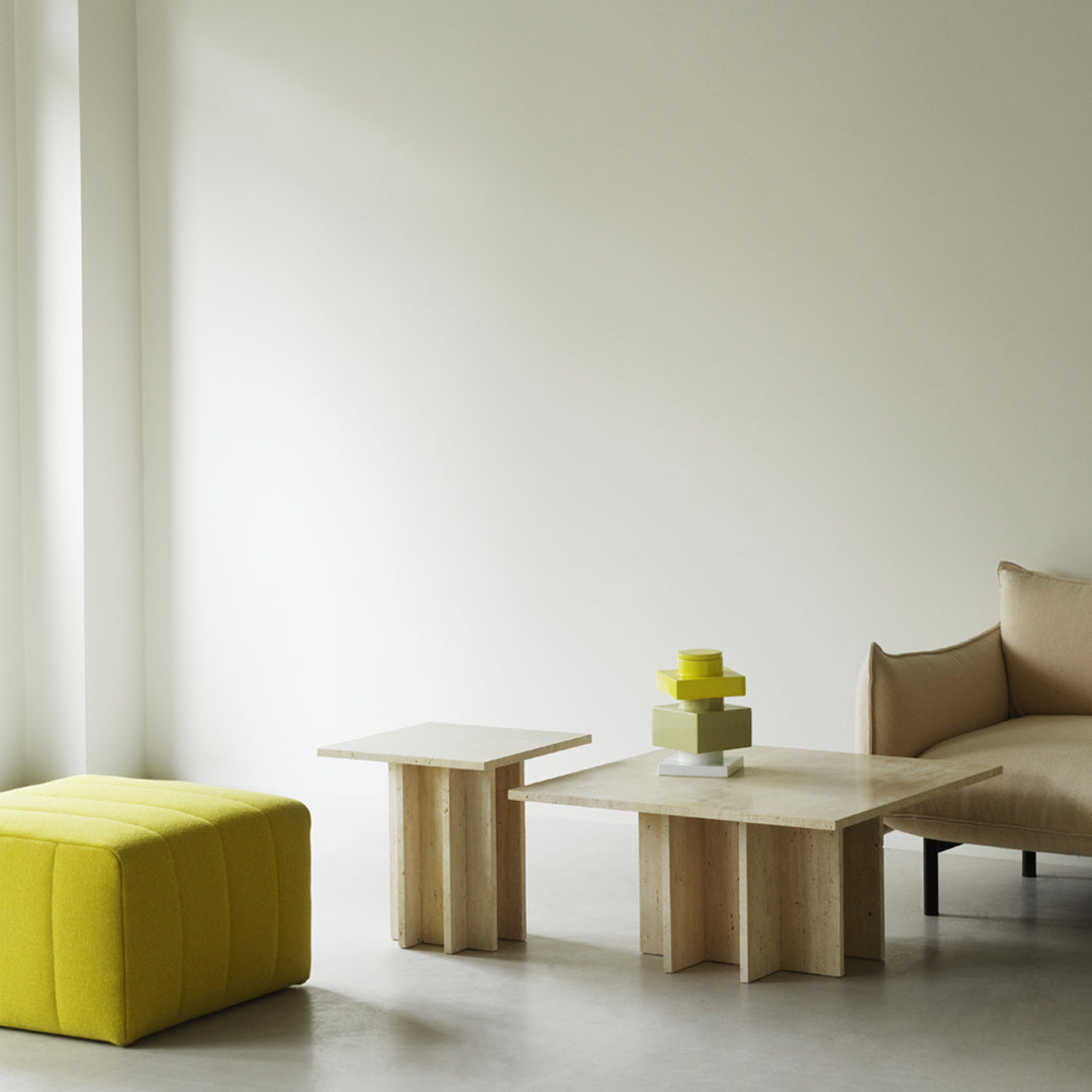Yellow ottoman, natural wood tables, and soft beige couch against a neutral wall, creating a modern, minimalist aesthetic.