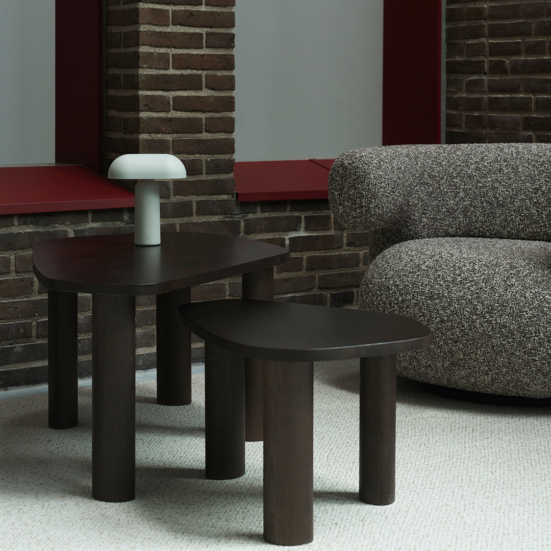 Dark wood side tables with curved edges, complemented by a soft gray, textured sofa and a white lamp.
