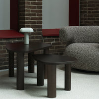 Dark wood side tables with curved edges, complemented by a soft gray, textured sofa and a white lamp.