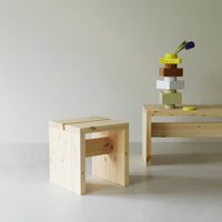 Natural wood stool with clean lines, paired with a minimalist wood table and colorful stacked blocks in yellow, green, and brown.