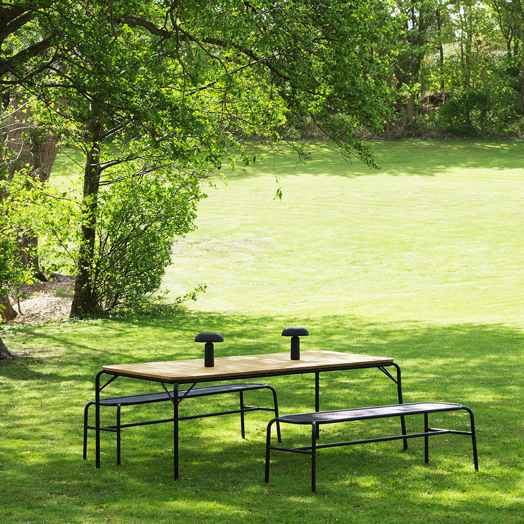 Outdoor black metal picnic table with wooden top and matching benches set against a lush green lawn.