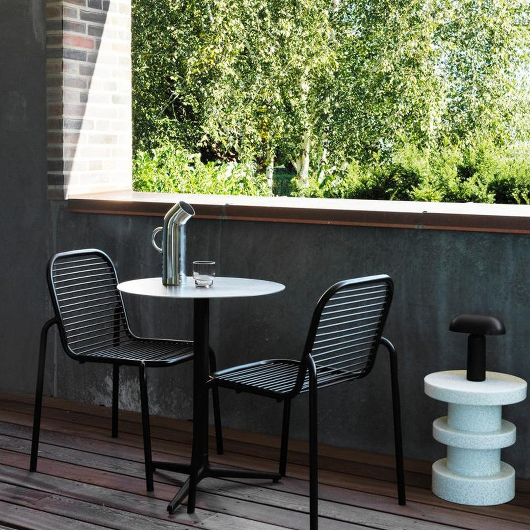 Black and white striped chairs paired with a round white table, set against a lush green background.