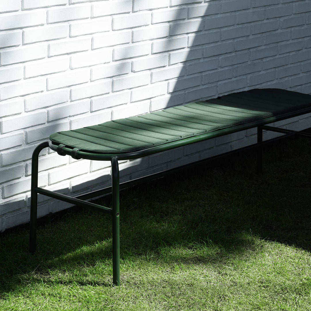 Green outdoor reclining lounge chair against a white brick wall, featuring a smooth, slatted design.