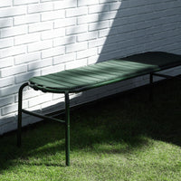 Green outdoor reclining lounge chair against a white brick wall, featuring a smooth, slatted design.