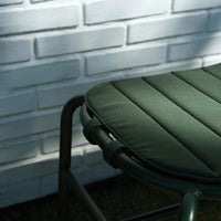 Green padded chair cushion with quilted pattern against a white brick wall.
