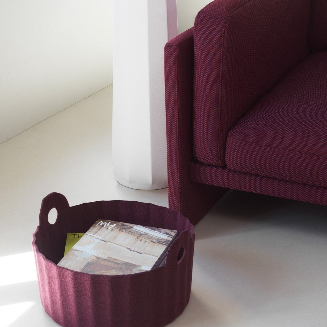 Burgundy round storage basket with textured fabric and a vibrant geometric pattern, beside a deep burgundy couch.