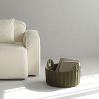Olive green storage basket with textured pattern, contrasting against a soft beige couch in a minimalistic setting.