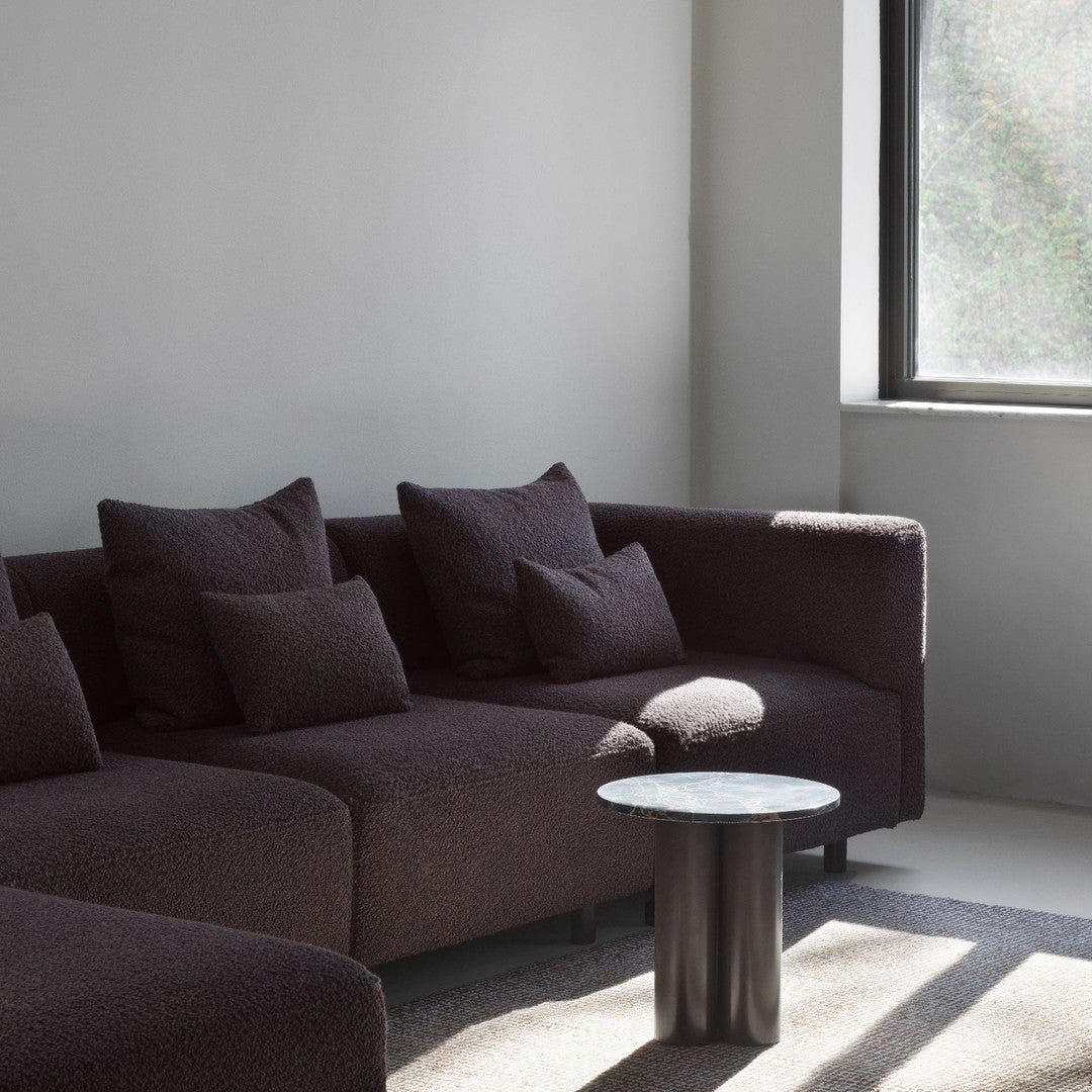 Textured dark brown sofa with matching pillows, set against a light gray wall and featuring a minimalist black table.