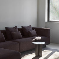 Textured dark brown sofa with matching pillows, set against a light gray wall and featuring a minimalist black table.