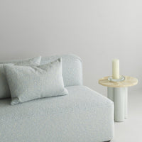 Soft blue textured sofa with light gray accents and decorative pillows, featuring a natural wood side table.