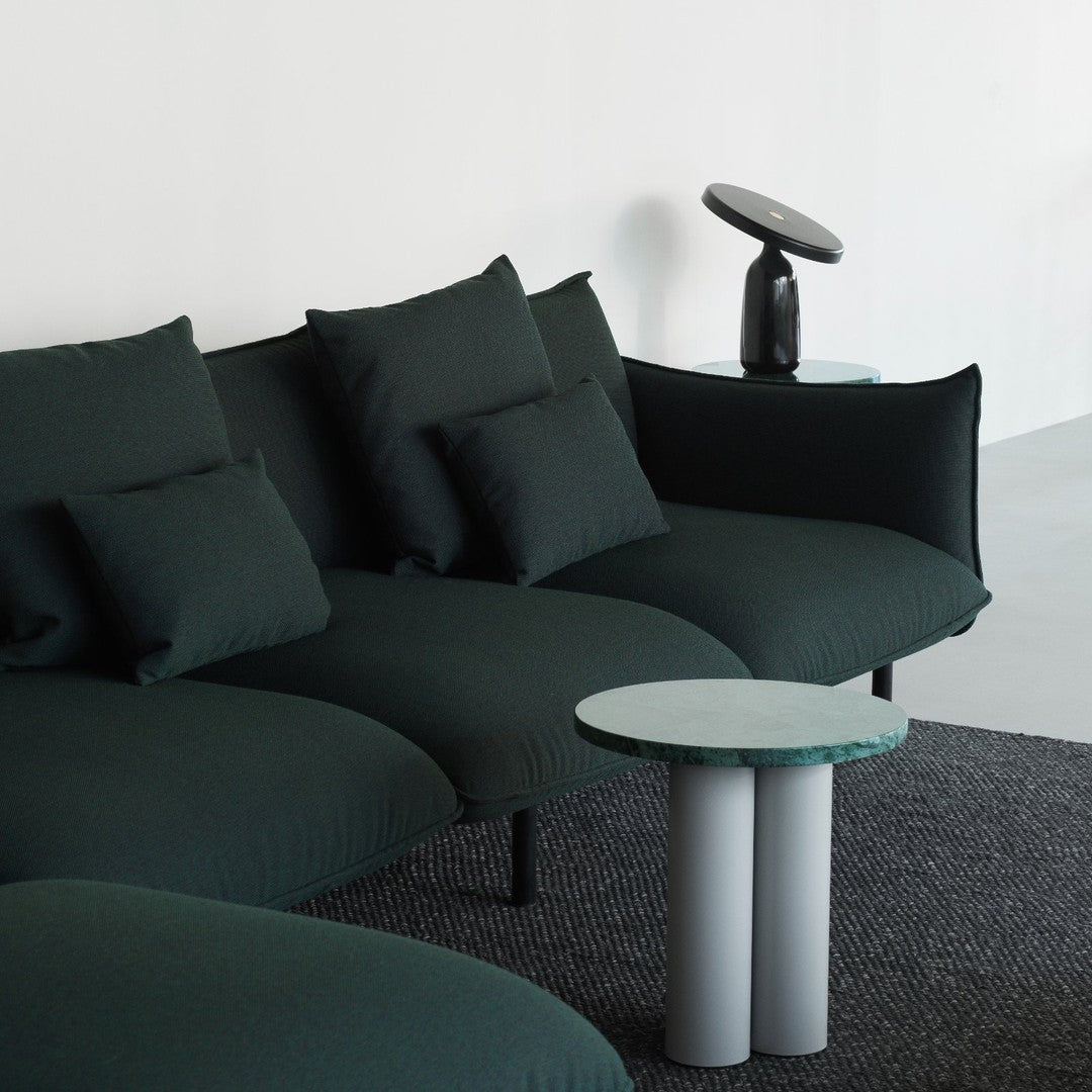 Dark green upholstered sofa with textured cushions, paired with a light gray and green marble side table on a black textured rug.
