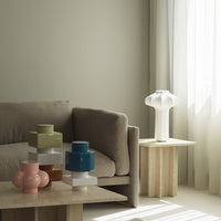 Colorful ceramic vases in green, blue, pink, and white, arranged on natural wood tables in a modern living space.