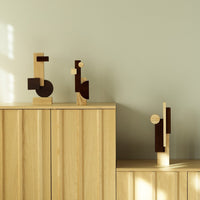Geometric wooden sculptures in natural oak and dark brown hues, set against a soft green wall.