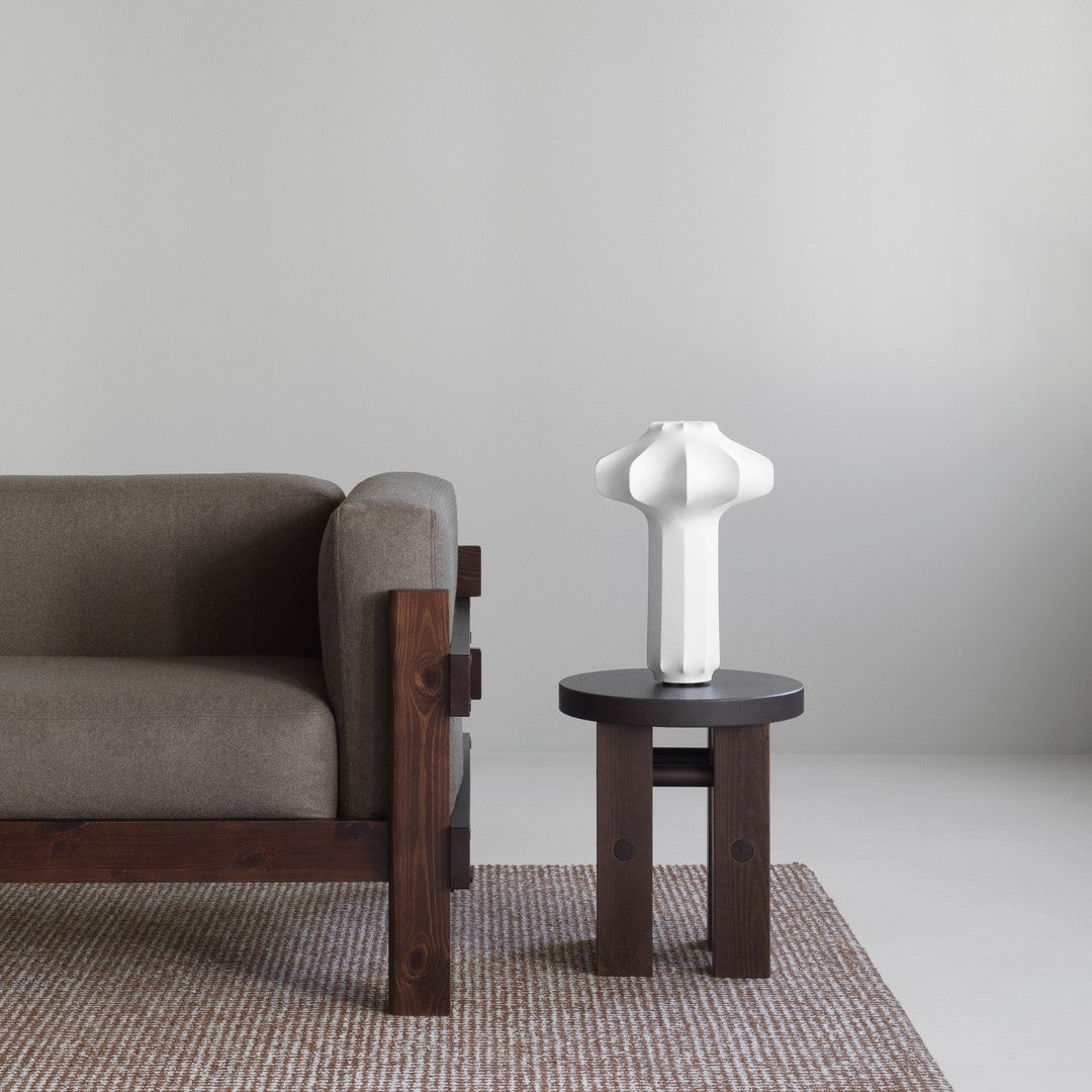 Gray sofa with a textured brown rug, white sculptural lamp on a dark wood table, minimalistic color palette.