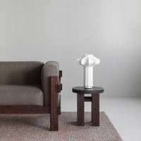 Gray sofa with a textured brown rug, white sculptural lamp on a dark wood table, minimalistic color palette.
