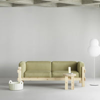 Green upholstered sofa with light wood frame, paired with white decor elements against a neutral background.