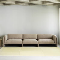 Beige upholstered sofa with soft, subtle texture against a light gray wall and a pale yellow rug. Modern minimalist design.