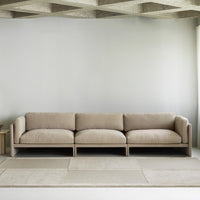 Beige modular sofa with a smooth texture and minimalist design, complemented by a light gray wall and soft rug tones.