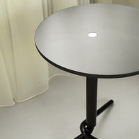 Modern round table with a sleek matte black base and a light gray top featuring a minimalist design.