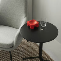 Gray upholstered chair beside a black round table with a bright red object, clear glass, and patterned rug.