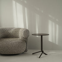 Gray textured sofa with a round black side table, set against a soft gray background. Elegant modern design.