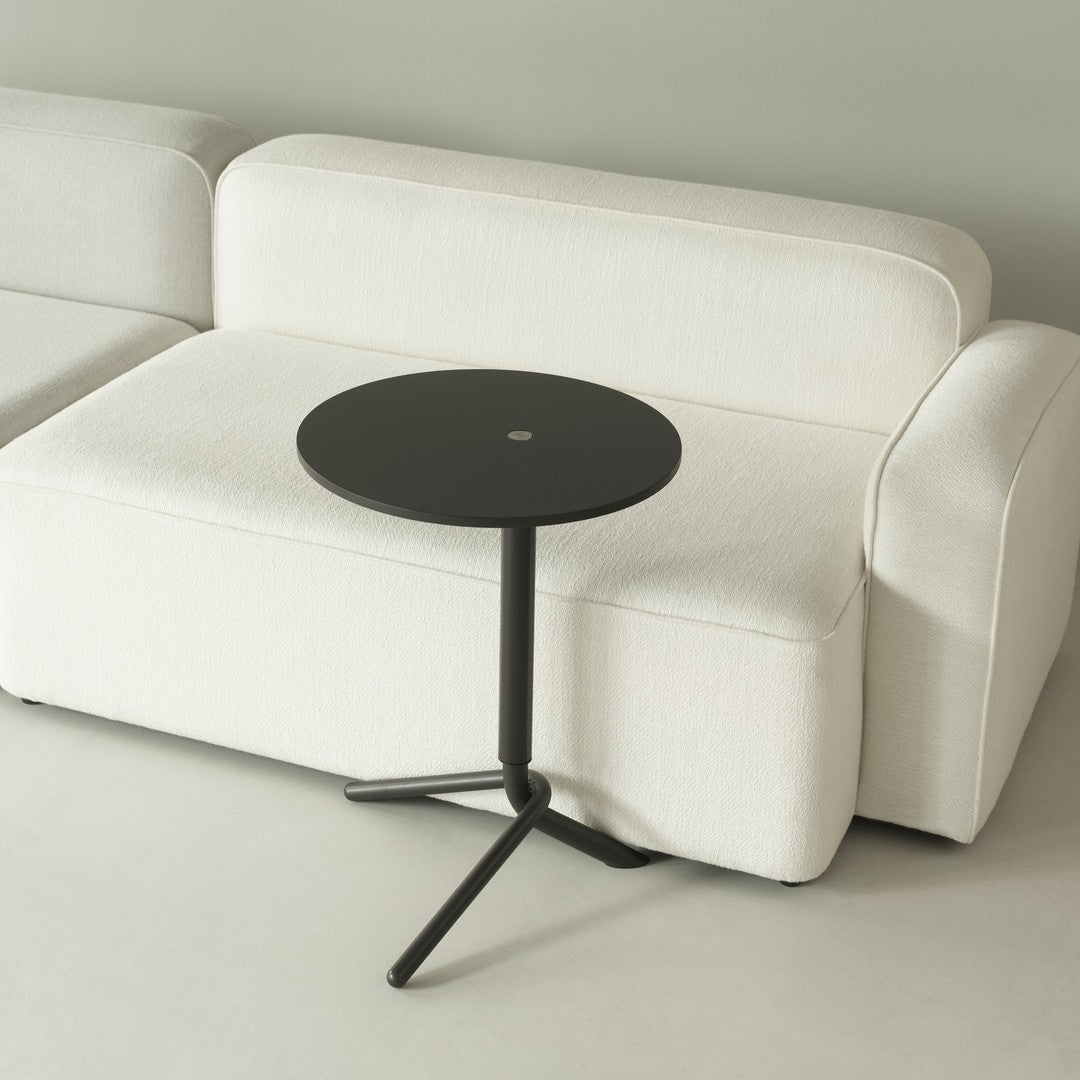 Minimalist black round side table paired with a cozy cream-colored couch, set against a neutral backdrop.