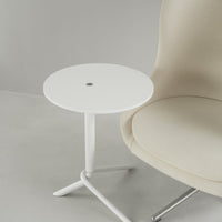 White round side table with a sleek metal base, paired with a soft beige upholstered chair in a minimalistic setting.