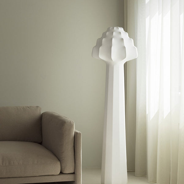 White sculptural lamp against a soft gray wall, complemented by a beige couch and sheer white curtains.