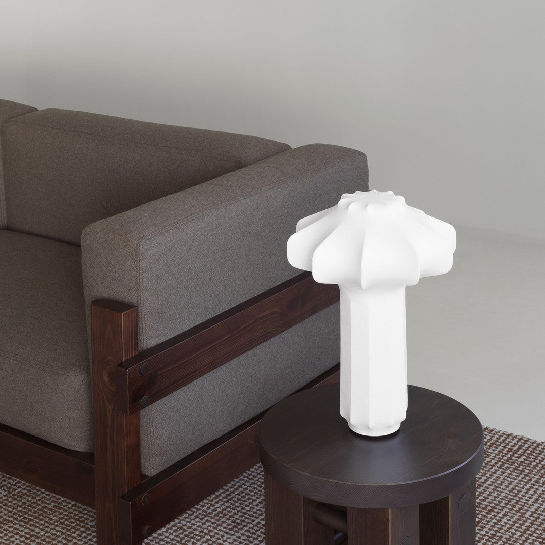 White textured lamp on a dark wood table, contrasting with a brown fabric sofa and light gray background.