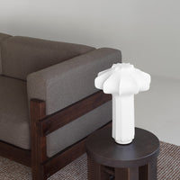 White textured lamp on a dark wood table, contrasting with a brown fabric sofa and light gray background.