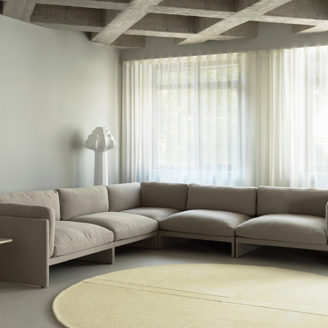 Beige modular sofa, soft yellow round rug, and sheer white curtains in a modern living space with gray accents.