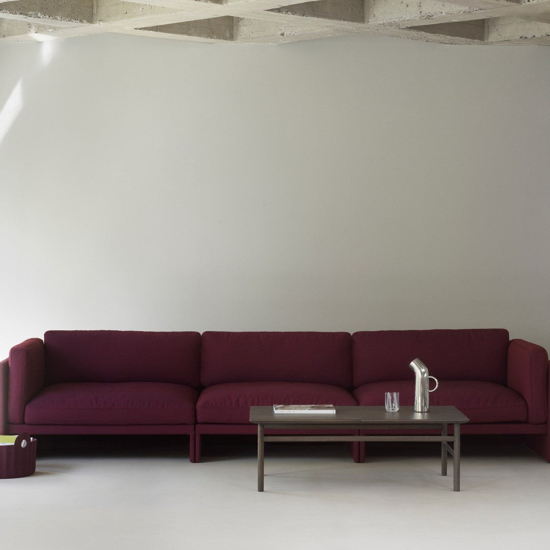 Burgundy sofa with a textured fabric, paired with a sleek wooden coffee table against a neutral gray backdrop.