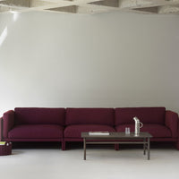 Burgundy sofa with a textured fabric, paired with a sleek wooden coffee table against a neutral gray backdrop.