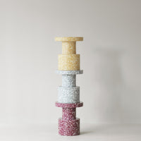 Colorful stacked decor in yellow, light blue, and burgundy with speckled patterns against a neutral background.