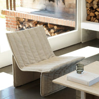 Beige quilted lounge chair with a minimalist design, featuring subtle texture against a modern interior backdrop.