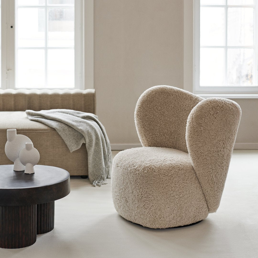 Beige plush chair with soft, rounded shapes, complemented by a gray throw and minimalist black table.