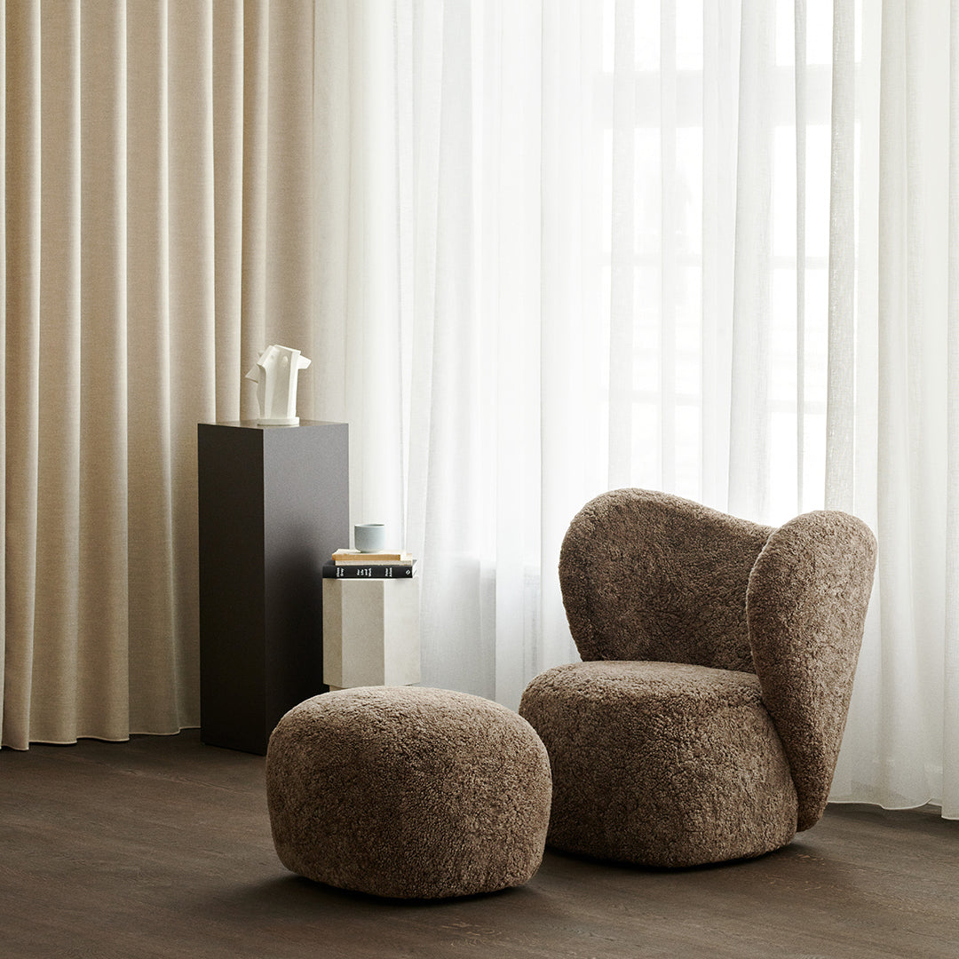 "Cozy brown boucle chair and ottoman in light-filled room with soft beige curtains."