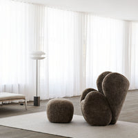Soft brown textured armchair and pouf in an airy, light-filled room with white curtains.